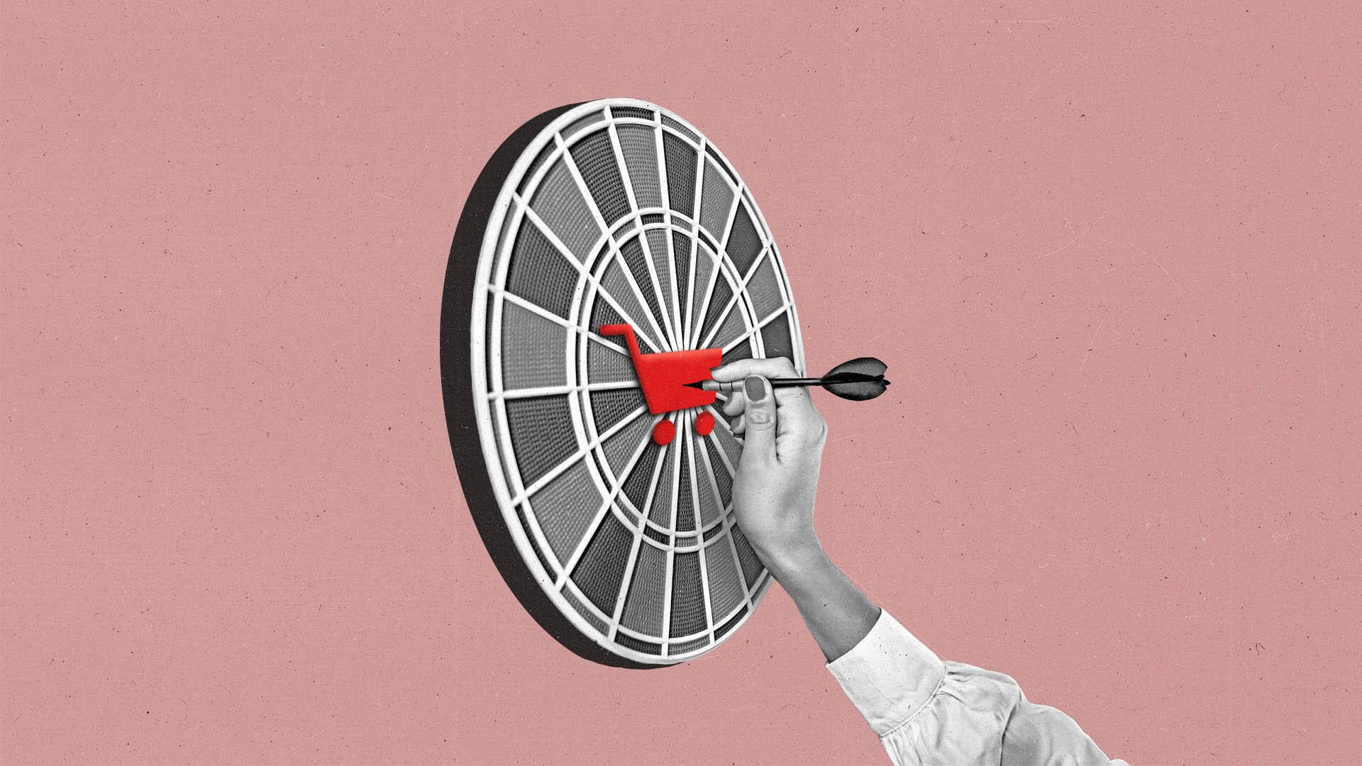 Hand pulls dart out of a dart board with a red shopping cart in the middle.