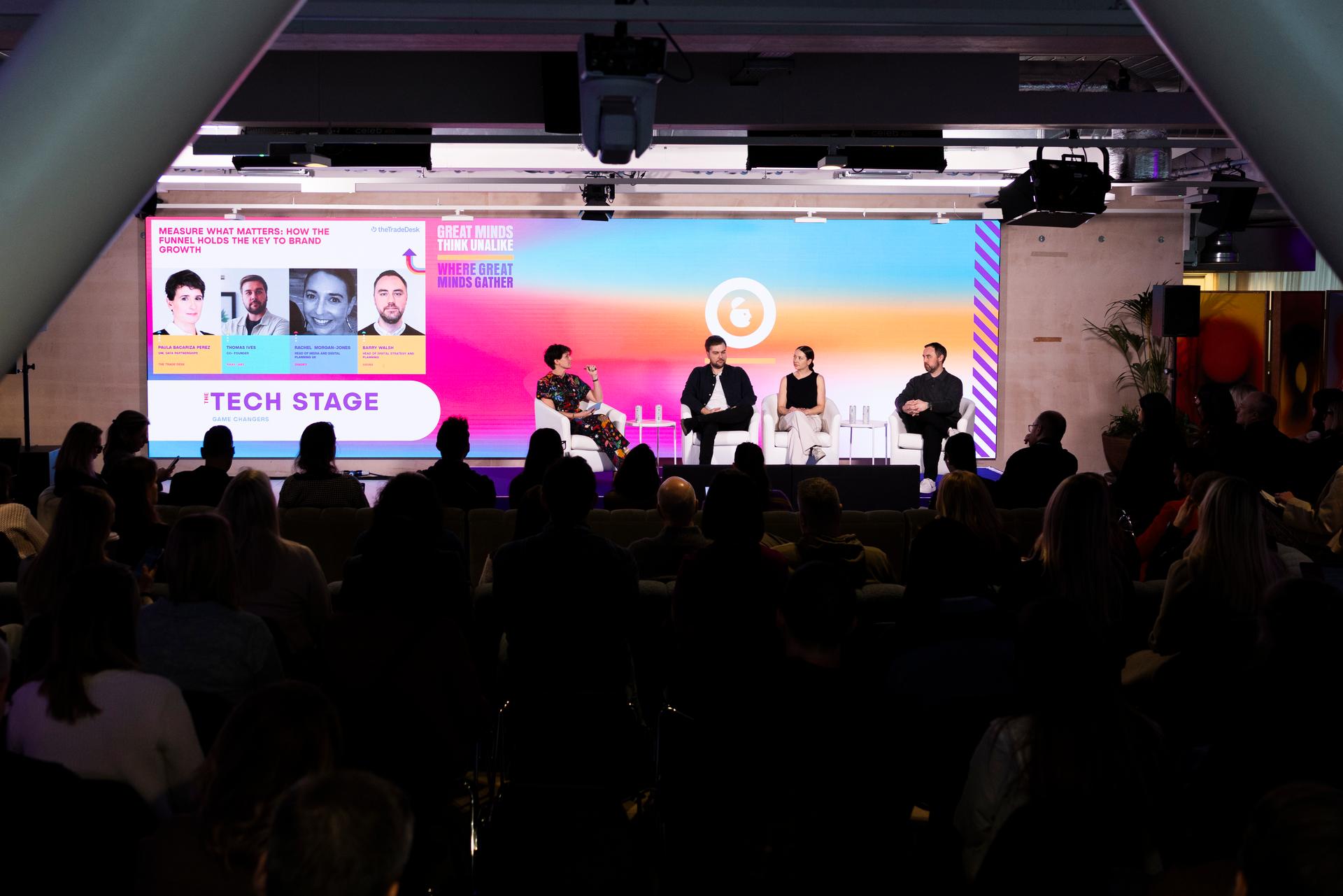 Panel discussion on the Tech Stage at Advertising Week Europe with four speakers seated on stage in front of a large colorful presentation screen and audience.