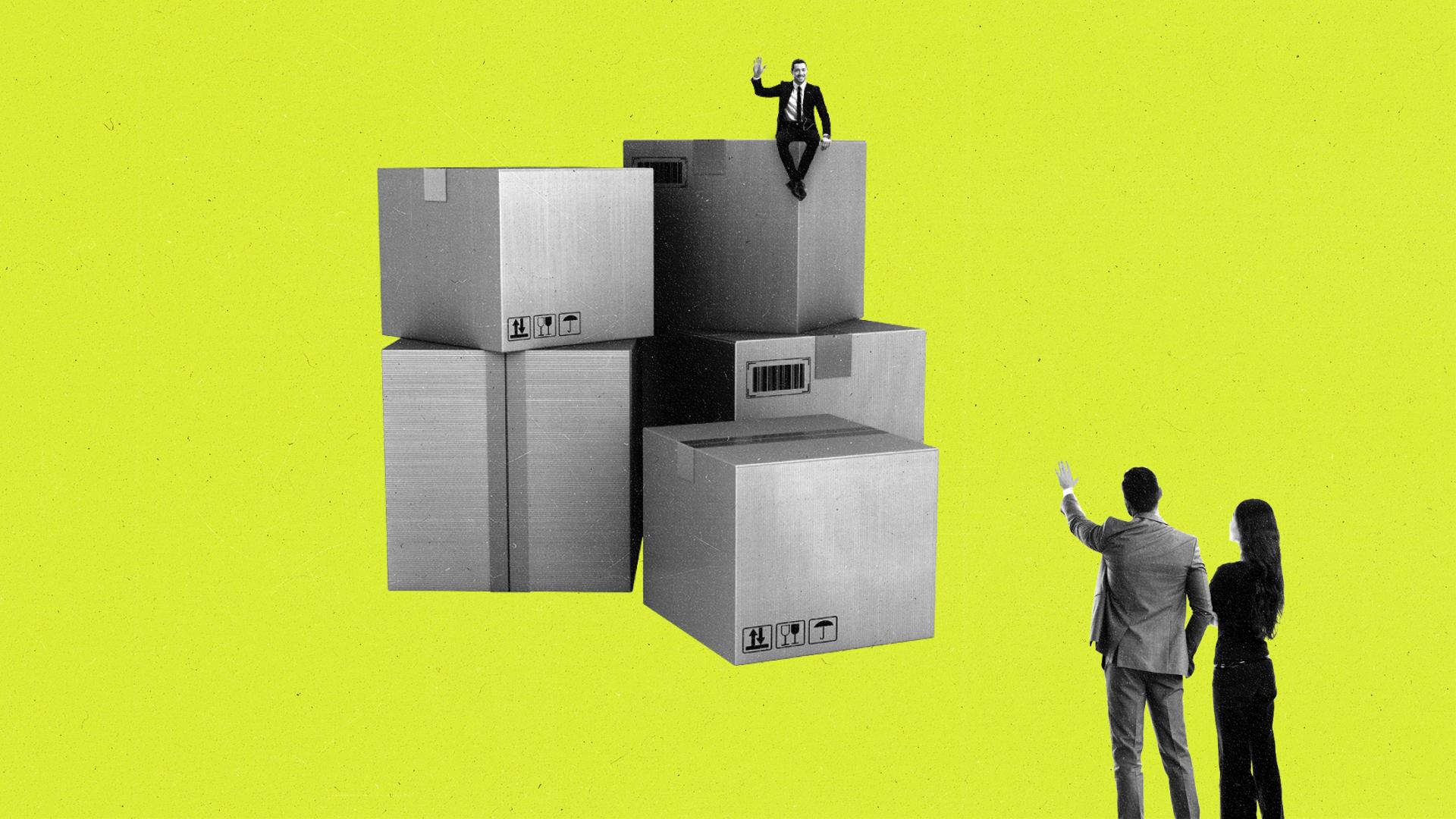 Miniature man sitting on cardboard boxes waves to a couple nearby.