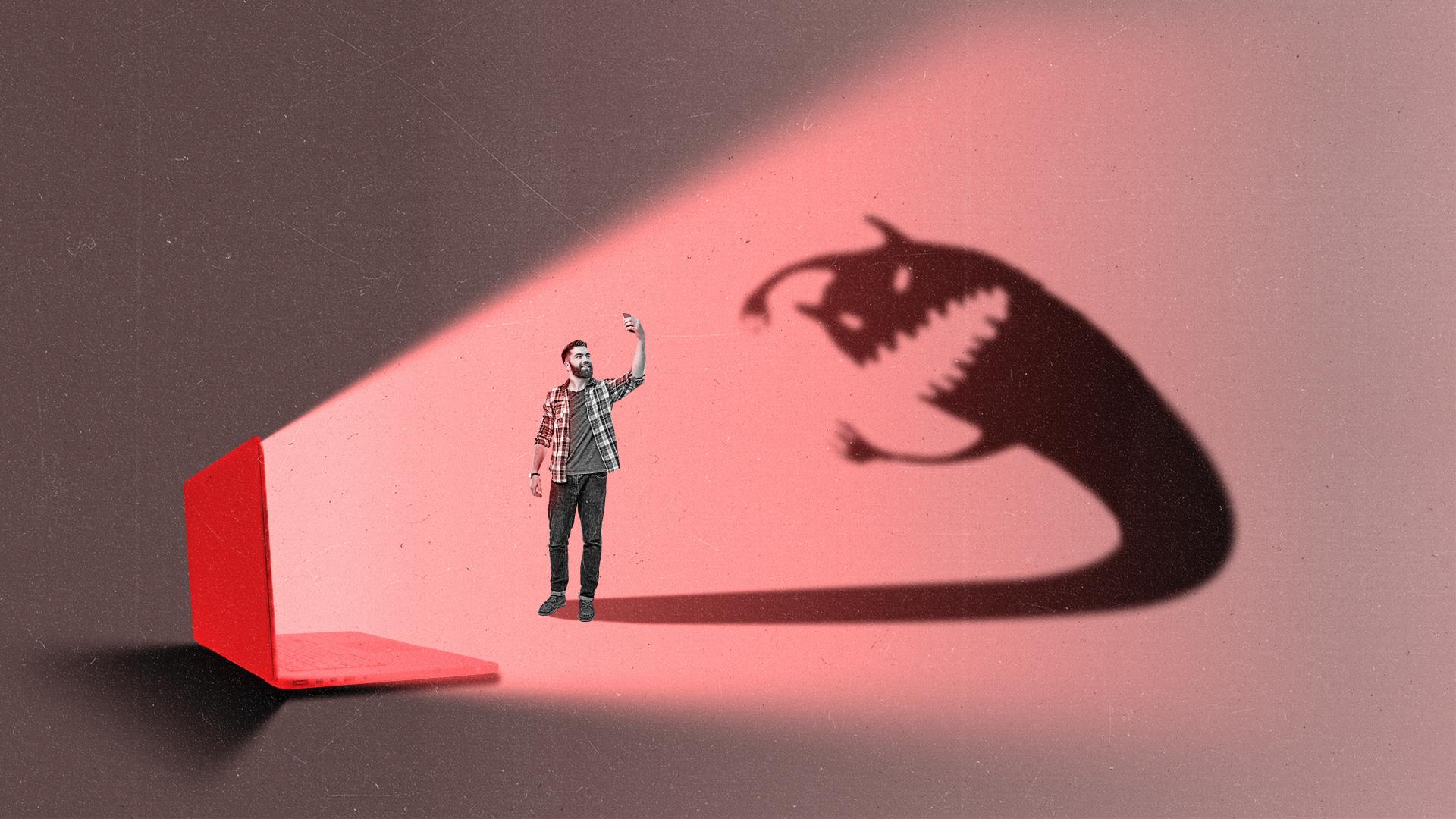 A computer shines its light at a person on their phone casting a shadow of a monster onto the wall.