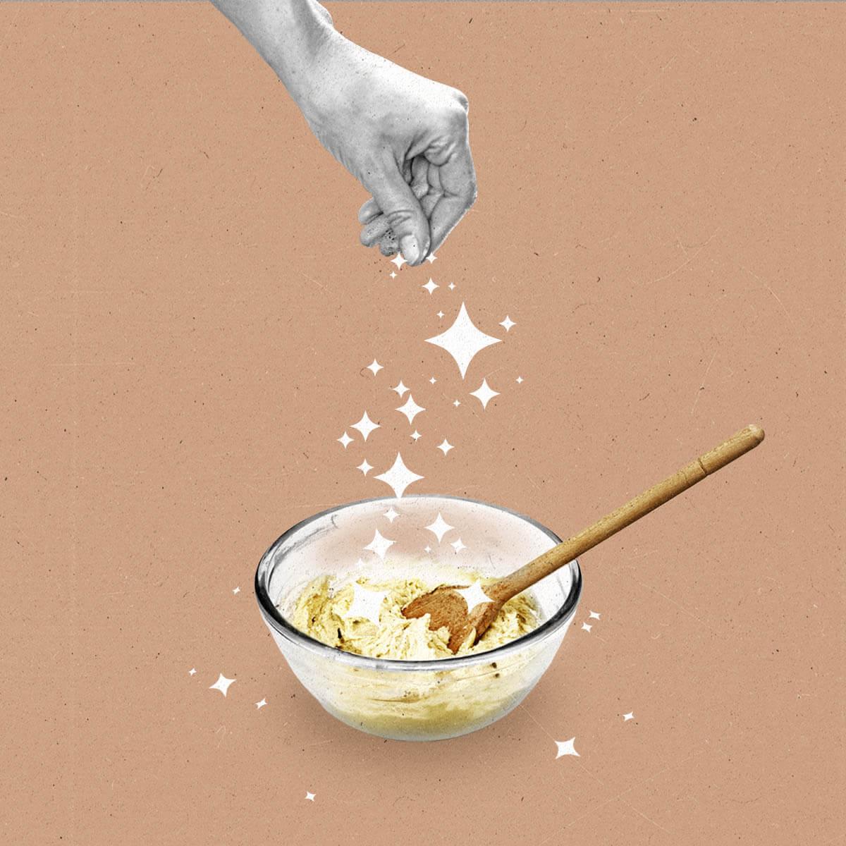 A hand sprinkles sparkles over a mixing bowl with dough in it.