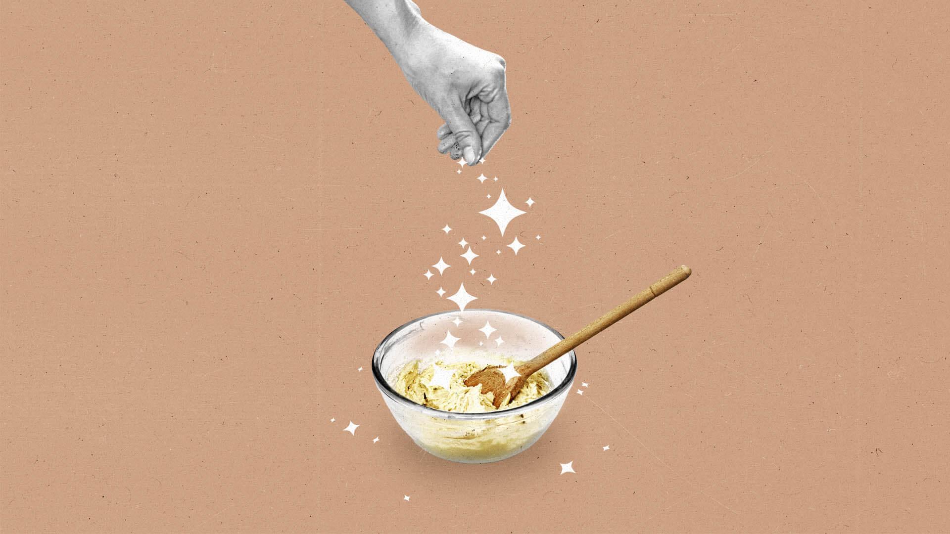 A hand sprinkles sparkles over a mixing bowl with dough in it.