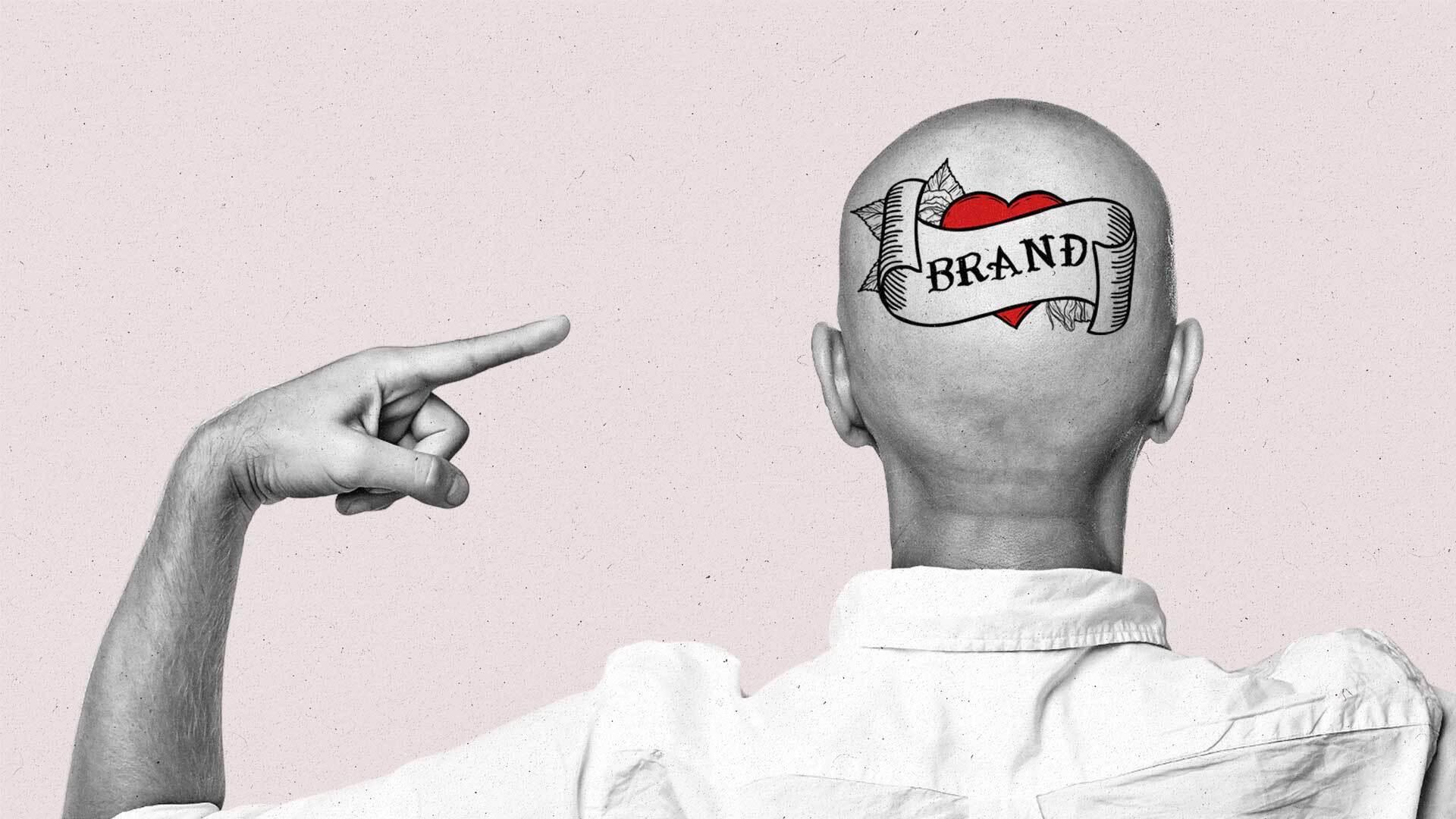 A bald man points at the "Brand" tattoo on the back of his head.