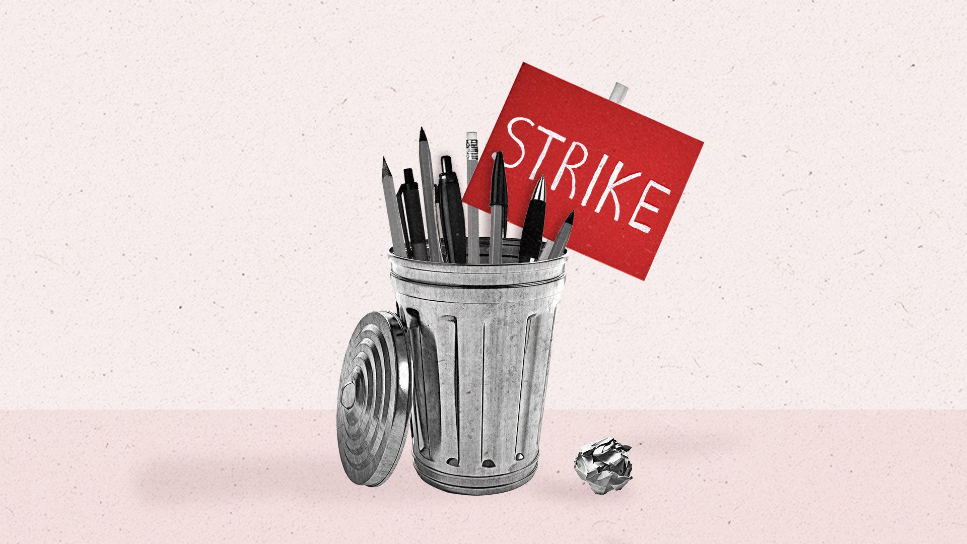 A bunch of pencils and pens sit inside a metal trashcan alongside a red picket sign that says 'STRIKE'.