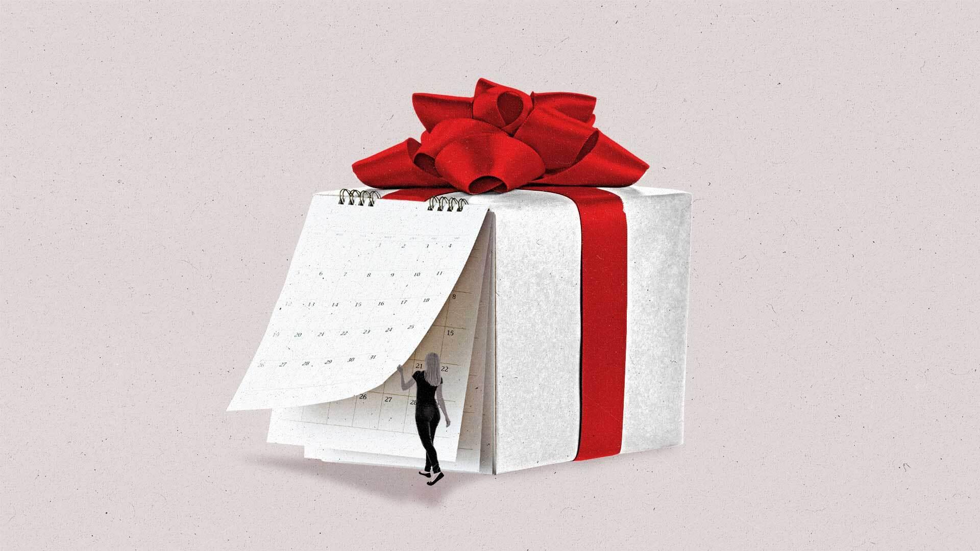 A woman turns the page of a calendar on the side of a large present with a red ribbon.