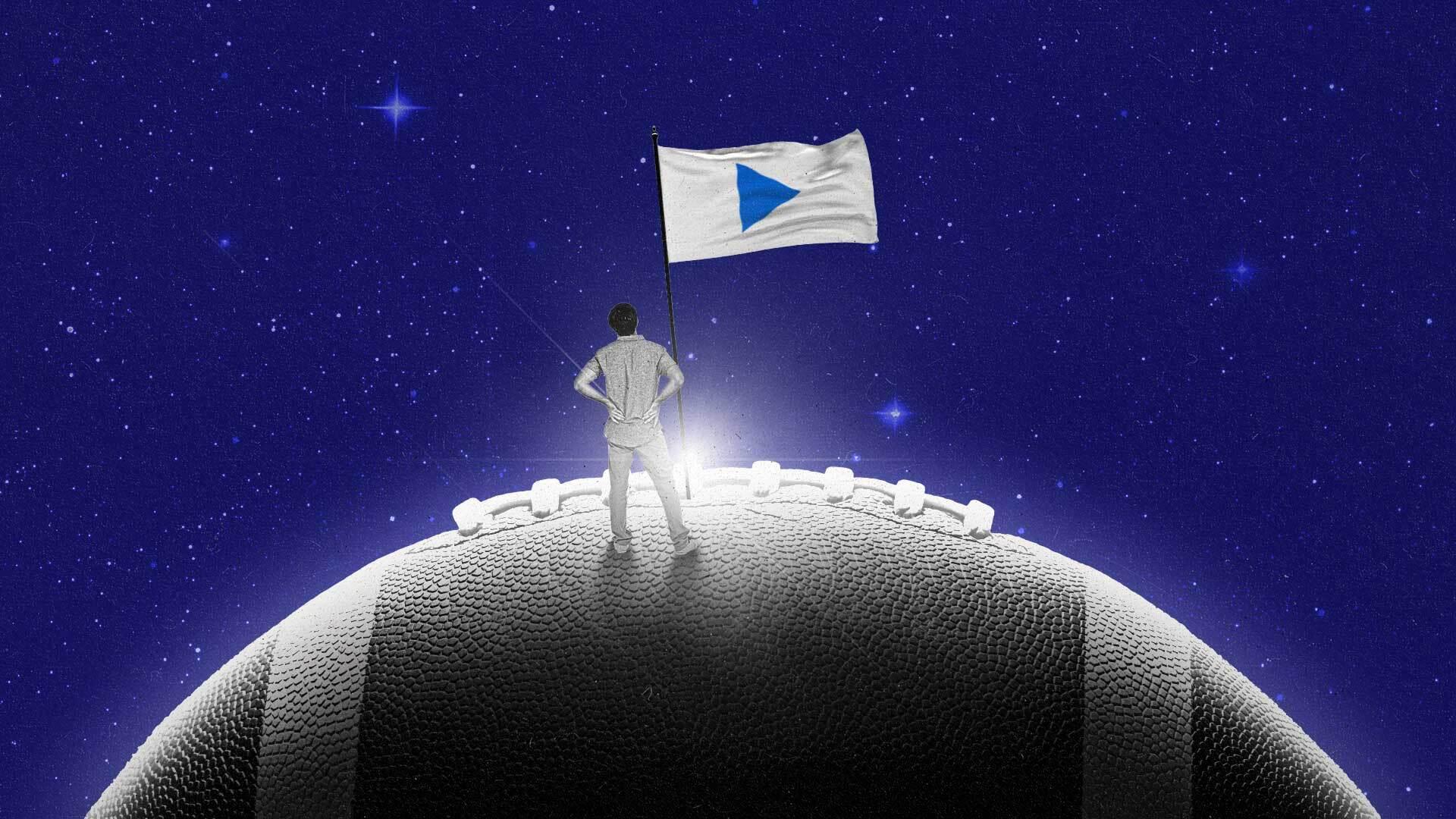 A small figure stands on a planet-sized football, marking it with a play-button flag.