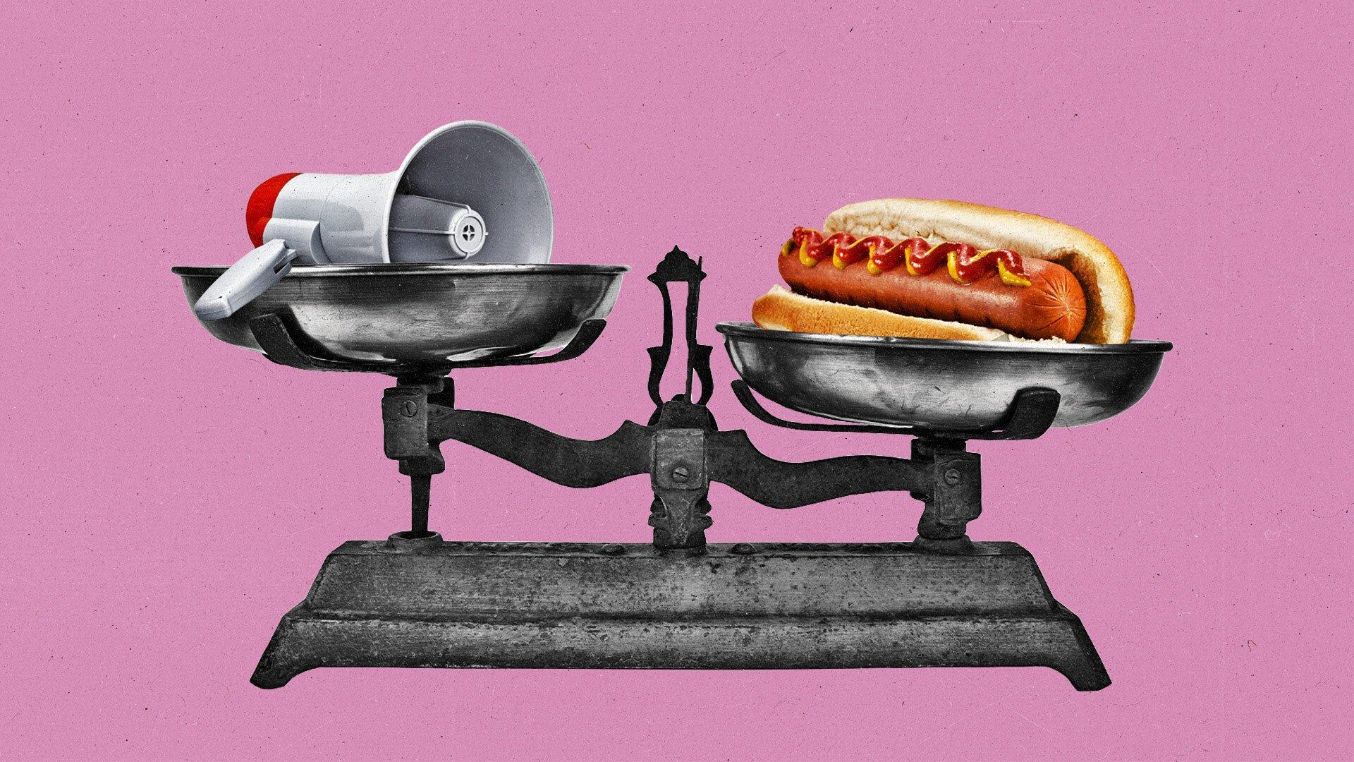 Scale with a hotdog on one side and a microphone on the other in front of a pink background.