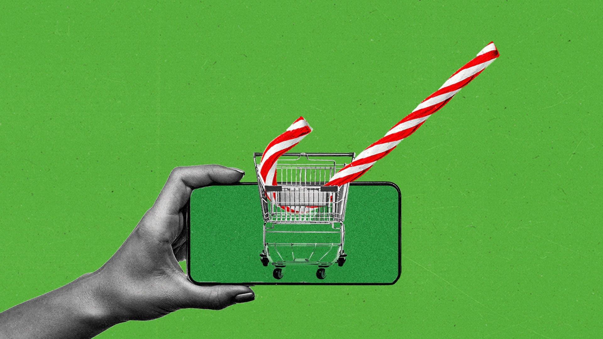 A hand holds a smartphone with the image of a shopping cart containing an oversized candy cane.