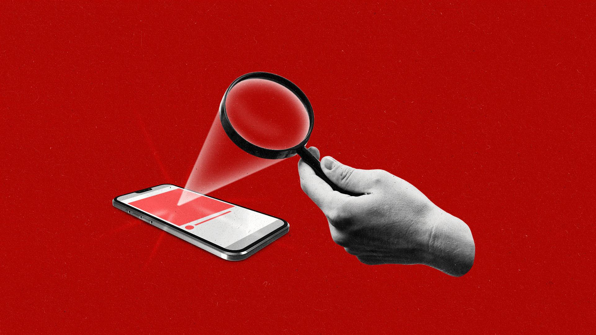 Hand holding a magnifying glass pointed towards a smartphone displaying an ad on the screen.